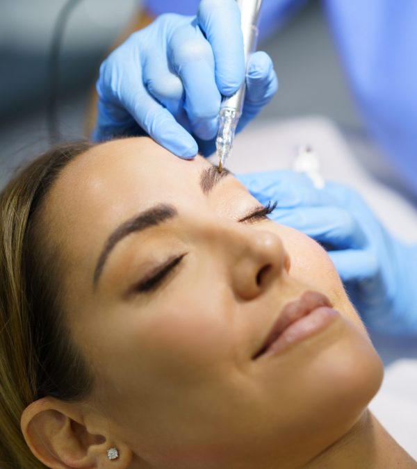 Permanent make-up for eyebrows of beautiful woman in a beauty salon. Close-up of beautician doing tattooing eyebrow. Micropigmentation treatment.