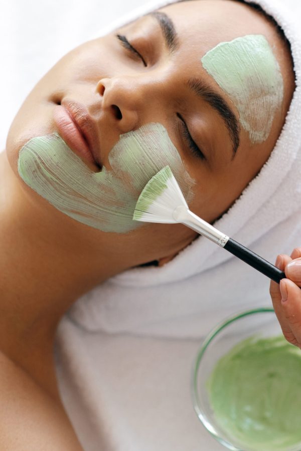 Skin care concept. Facial treatments, facial cleansing. Close-up of beauty procedure, therapist applying green face mask on half face of a beautiful brazilian or hispanic young woman